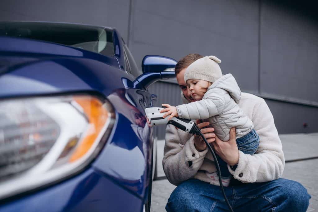 father playing with daughter while charging electric car